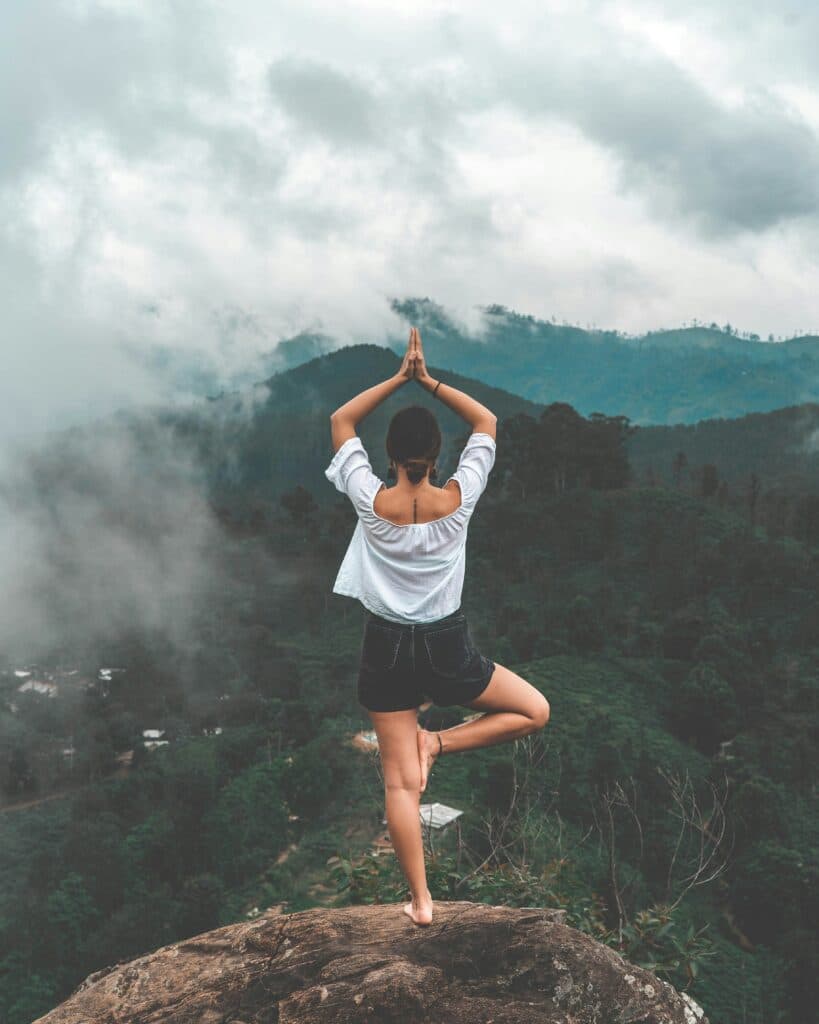woman doing yoga on the top of a mountain surrounded by trees and clouds